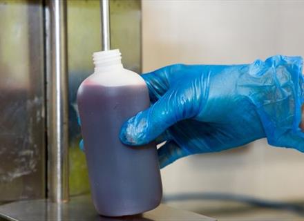 a hand with a blue glove doing liquid filling using a machine