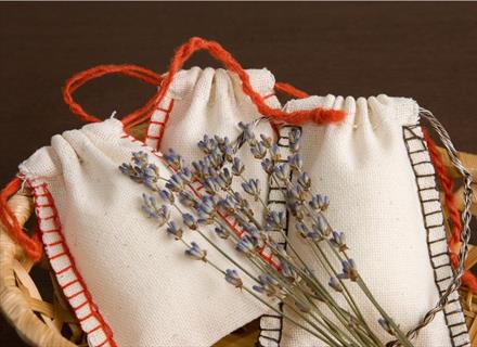 a hand holding a scented sachet next to flowers and a mortar and pestle