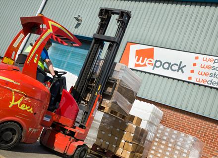 A man in a forklift in front of an order of products in cardboard boxes